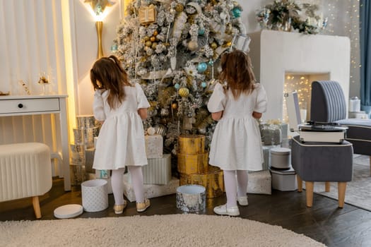 Two twin sisters in a white dress decorate the Christmas tree with their own hands, Christmas holidays at home