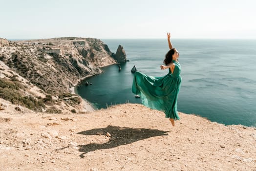 Woman green dress sea. Female dancer posing on a rocky outcrop high above the sea. Girl on the nature on blue sky background. Fashion photo