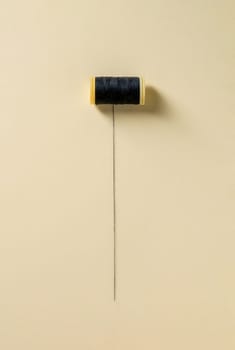 Black sewing thread wrapped around a partially unwrapped plastic spool on a yellow background