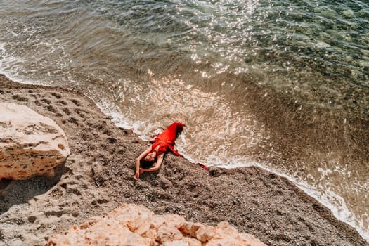 Woman red dress sea. Female dancer in a long red dress posing on a beach with rocks on sunny day.