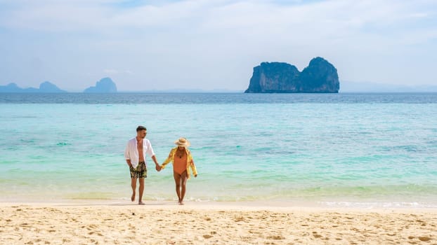 a couple walking at the tropical beach of Koh Ngai island, men and woman by the ocean with on the background tropical limestone cliffs islands of the Andaman sea