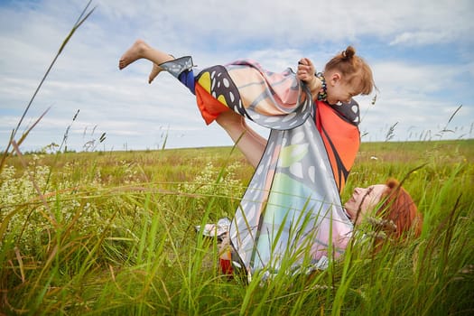 Happy female family with mother and daughter on green and yellow meadow full of grass and flower. Woman with red hair and blonde girl having fun, joy and hug in sunny summer day. Concept family love