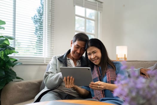 Retired elderly couple sits on couch using tablet together and relax in their home. Senior Activity Concept.