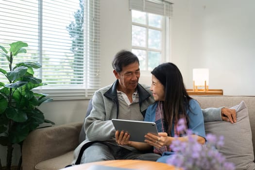 Retired elderly couple sits on couch using tablet together and relax in their home. Senior Activity Concept.