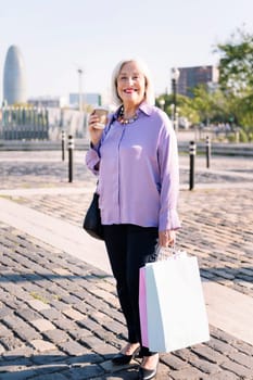 senior woman smiling standing with shopping bags and a takeaway coffee, concept of elderly people leisure and active lifestyle