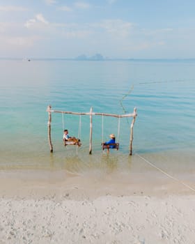 a couple of men and a woman on a swing at the beach of Koh Muk or Koh Mook Trang Thailand, a couple on a swing in the ocean