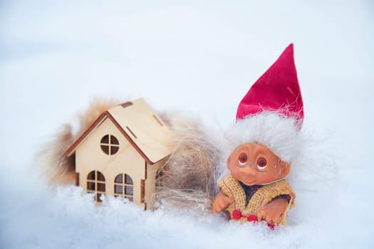 Cute little funny dwarf and small wooden house in snow in winter landscape. Wizard on snowy background. Christmas and New Year