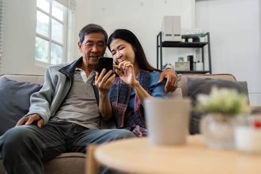 Retired elderly couple sits on couch drink tea and using mobile together and relax in their home. Senior Activity Concept.