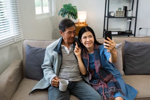 Retired elderly couple sits on couch drink tea and using mobile together and relax in their home. Senior Activity Concept.