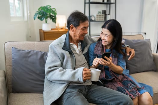 Retired elderly couple sits on couch drink tea and using mobile together and relax in their home. Senior Activity Concept.