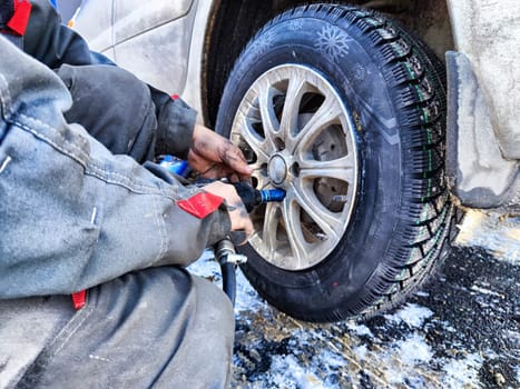 Ishim, Russia - November 27, 2023: man makes tire of car wheel before cold snow season. Experienced mechanic changes wheel of car. The driver prepares a classic car for driving in the snow in winter