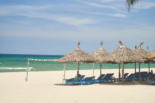 Straw sunshades and sunbeds on the empty pebble beach with sea in the background. Deserted beach with rattan sun loungers and umbrellas