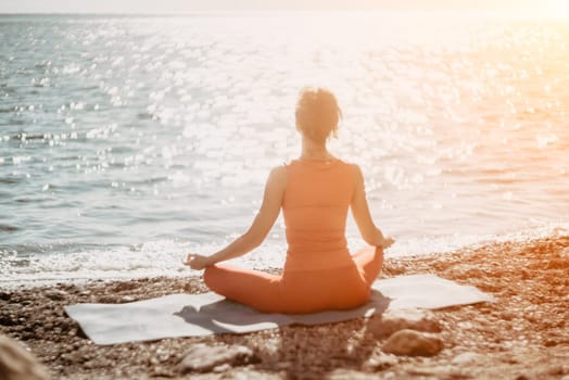 The woman in a red suit practicing yoga on stone at sunrise near the sea. Young beautiful girl in a red bathing suit sits on the seashore in lotus position. Yoga. Healthy lifestyle. Meditation