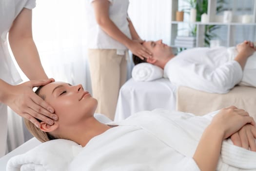 Caucasian couple enjoying relaxing anti-stress head massage and pampering facial beauty skin recreation leisure in dayspa modern light ambient at luxury resort or hotel spa salon. Quiescent