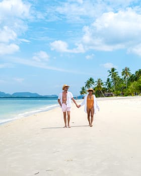 a young couple of caucasian men and a Thai Asian woman walking at the beach o Koh Muk a tropical island, with palm trees soft white sand, and a turqouse colored ocean, Koh Mook Trang Thailand