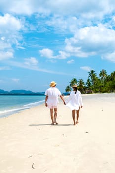 a young couple of caucasian men and a Thai Asian woman walking at the beach o Koh Muk a tropical island, with palm trees soft white sand, and a turqouse colored ocean, Koh Mook Trang Thailand