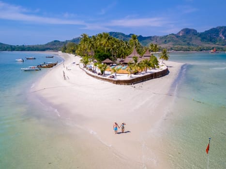 a couple of men and woman walking at the beach during a tropical vacation in Thailand, Koh Muk a tropical island with palm trees soft white sand, and a turqouse colored ocean in Thailand