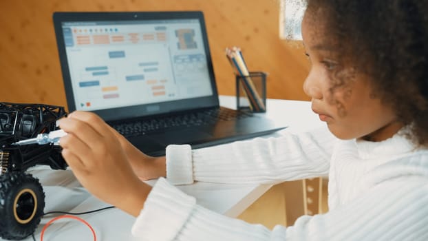 Smart african girl build robotic car while using wires while using laptop setting or writing prompt code. Skilled female student working on computer in STEM technology online classroom. Erudition.