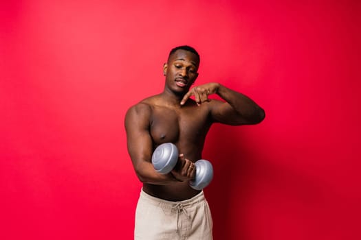 Young man with dumbbells good physique isolated on red black background. Strength and motivation