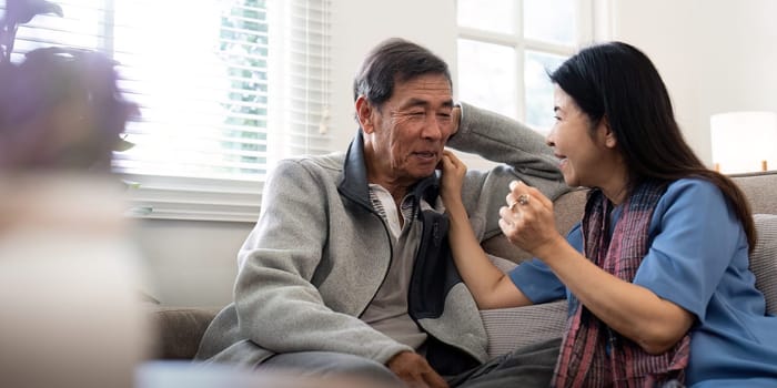 Happy mature husband and wife sit rest on comfortable sofa in living room enjoy talking, smiling elderly couple relax on couch at home chat speak laugh on leisure weekend.