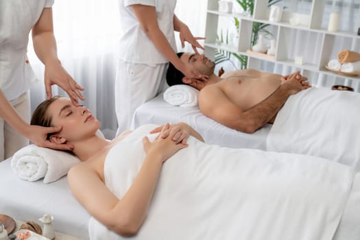 Caucasian couple enjoying relaxing anti-stress head massage and pampering facial beauty skin recreation leisure in dayspa modern light ambient at luxury resort or hotel spa salon. Quiescent