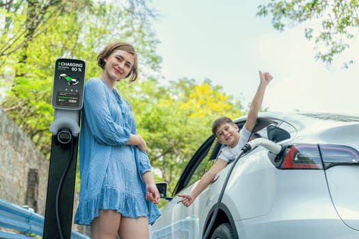 Family road trip vacation with electric vehicle, mother and son recharge EV car with green and clean energy. Nature and travel with eco-friendly car for sustainable environment. Perpetual