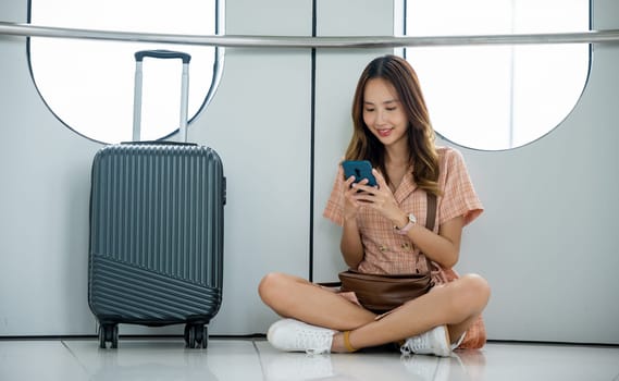 Traveler enjoying a moment of relaxation with her smartphone, luggage, and backpack in the airport terminal before her flight. travel in vacation summer