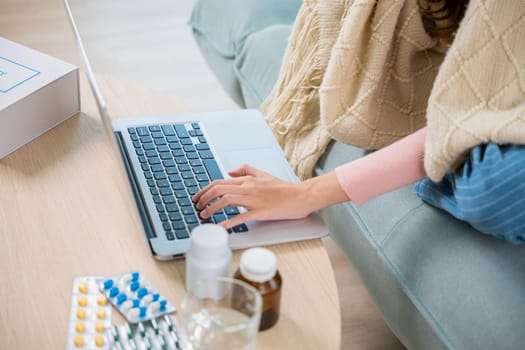 Sick young woman sit on sofa video call online with laptop consult with doctor at home, female covered blanket checking medications online, healthcare and technology