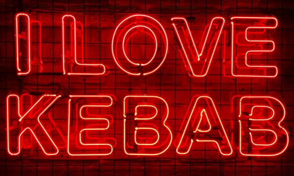 Neon shining sign in red color on a brick wall in the dark with the inscription or slogan I love kebab. Brick wall, background. Bright electric neon light. Cafe-restaurant Doner Kebab