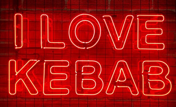 Neon shining sign in red color on a brick wall with the inscription or slogan I love kebab. Brick wall, background. Bright electric neon light. Cafe-restaurant Doner Kebab