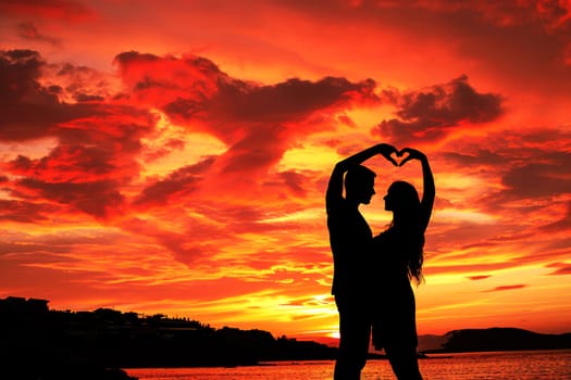 A couple of love makes a heart-shaped gesture, while the sunset. AI Background.