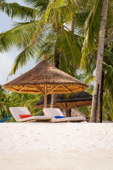 Wooden beach parasol and beach loungers at sunset.Luxury beach umbrella at luxurious beach resort. Summer beach concept,carefree, rest seaside,Nobody on the beach.Palm on the back.