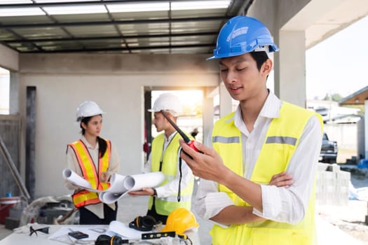 Portrait of a male engineer at a construction site using a walkie-talkie. Standing in charge of planning a construction project in formal attire, wearing a hard hat, a successful civil engineer..