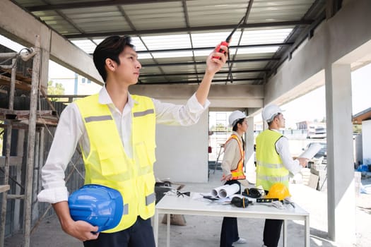 Portrait of a male engineer at a construction site using a walkie-talkie. Standing in charge of planning a construction project in formal attire, wearing a hard hat, a successful civil engineer..