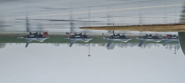Armed American fighter jets, poised for immediate takeoff, under pouring rain, their silhouettes reflecting off the runway puddles, showcasing readiness in any weather.