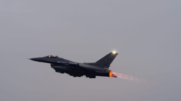 USAF fighter jet ignites its afterburner to full thrust at takeoff, the bright flame contrasting sharply against the grey sky. Ideal for editorial content. Copy space.