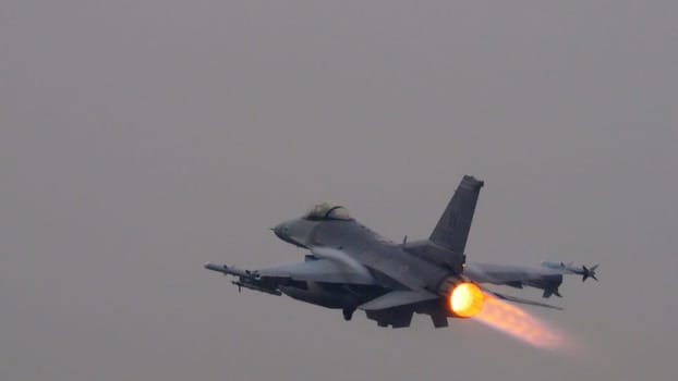 USAF fighter jet ignites its afterburner to full thrust at takeoff, the bright flame contrasting sharply against the grey sky. Ideal for editorial content. Copy space.