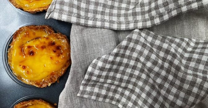 Lots of freshly baked Pastel de nata or Portuguese egg tart desserts in a baking dish. Pastel de Belme is a small pie with a crispy puff pastry crust and a custard filling. Small cupcake