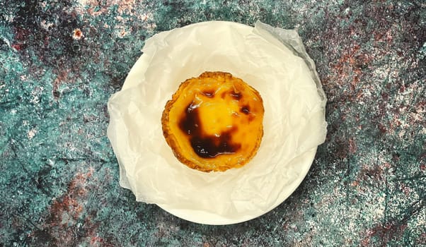 One Pastel de nata or Portuguese egg tart on a white plate. Pastel de Belm is a small pie with a crispy puff pastry crust and a custard cream filling