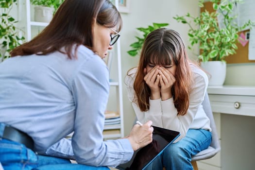 Sad, crying teenage girl at a session in the office of a mental professional, psychologist, counselor, social worker. Feelings, difficulties, problems, depression, stress, youth concept