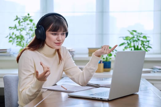 Teenage girl college student in headphones having video conference chat online meeting lesson webinar on computer laptop screen, sitting at desk at home. E-learning, education, technology, knowledge