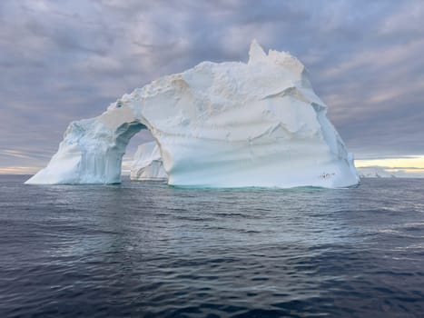 A huge high breakaway glacier drifts in the southern ocean off the coast of Antarctica at sunset, the Antarctic Peninsula, the Southern Arctic Circle, azure water, cloudy weather. High quality photo