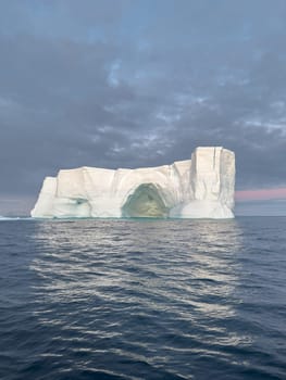 A huge high breakaway glacier drifts in the southern ocean off the coast of Antarctica at sunset, the Antarctic Peninsula, the Southern Arctic Circle, azure water, cloudy weather. High quality photo