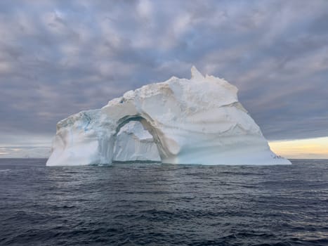 A huge high breakaway glacier drifts in the southern ocean off the coast of Antarctica at sunset, the Antarctic Peninsula, the Southern Arctic Circle, azure water, cloudy weather. High quality photo