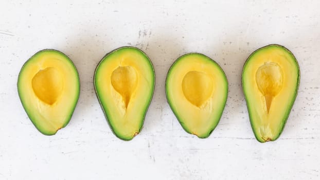 Four avocado halves with bright yellow pulp on white stone board, view from above