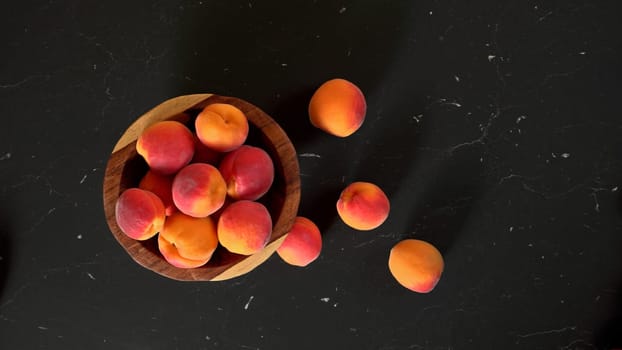 Top down view, small wooden bowl with apricots, some spilled on dark marble like board under