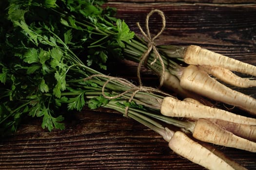 Fresh parsnip roots with green leaves on dark wooden board