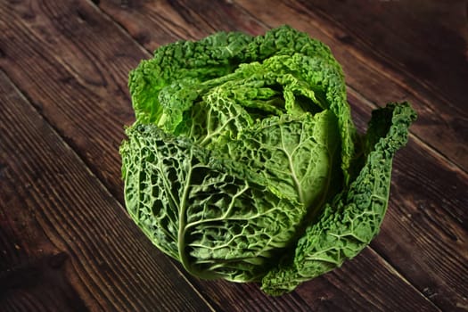 Green savoy cabbage head on dark wooden board