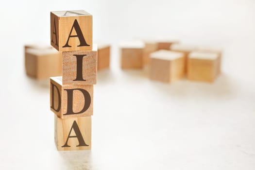 Four wooden cubes arranged in stack with letters AIDA (meaning Awareness Interest Desire Action) on them, space for text / image at down right corner