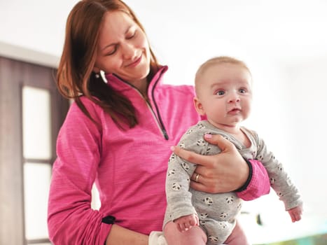 Mother holds infant baby boy son in her hands, as she plays with him